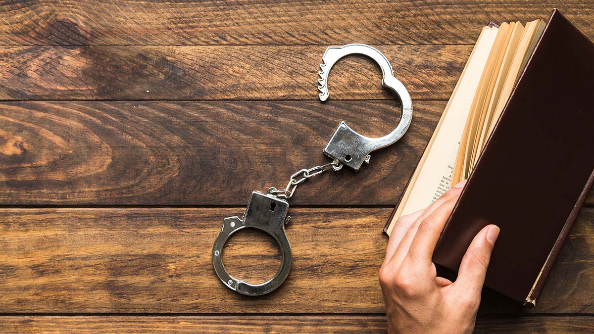 Código de Processo Penal sendo estudado com livro aberto e algemas sobre a mesa.